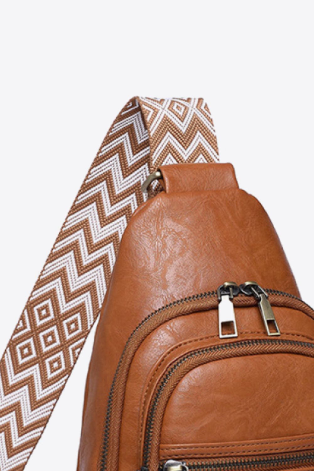 Brown leather sling bag with geometric patterned strap and double zipper detail.
