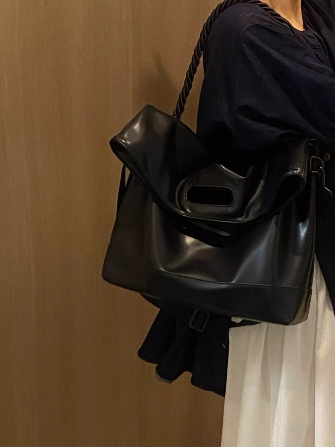 Black oversized PU leather tote bag with unique cut-out handle and rope strap.