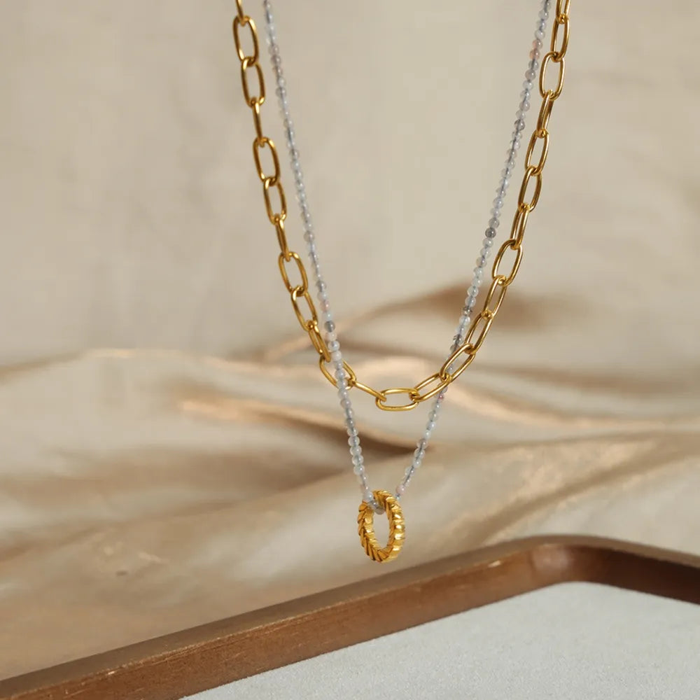 Gold layered chain and beaded pendant necklace with a textured ring detail.