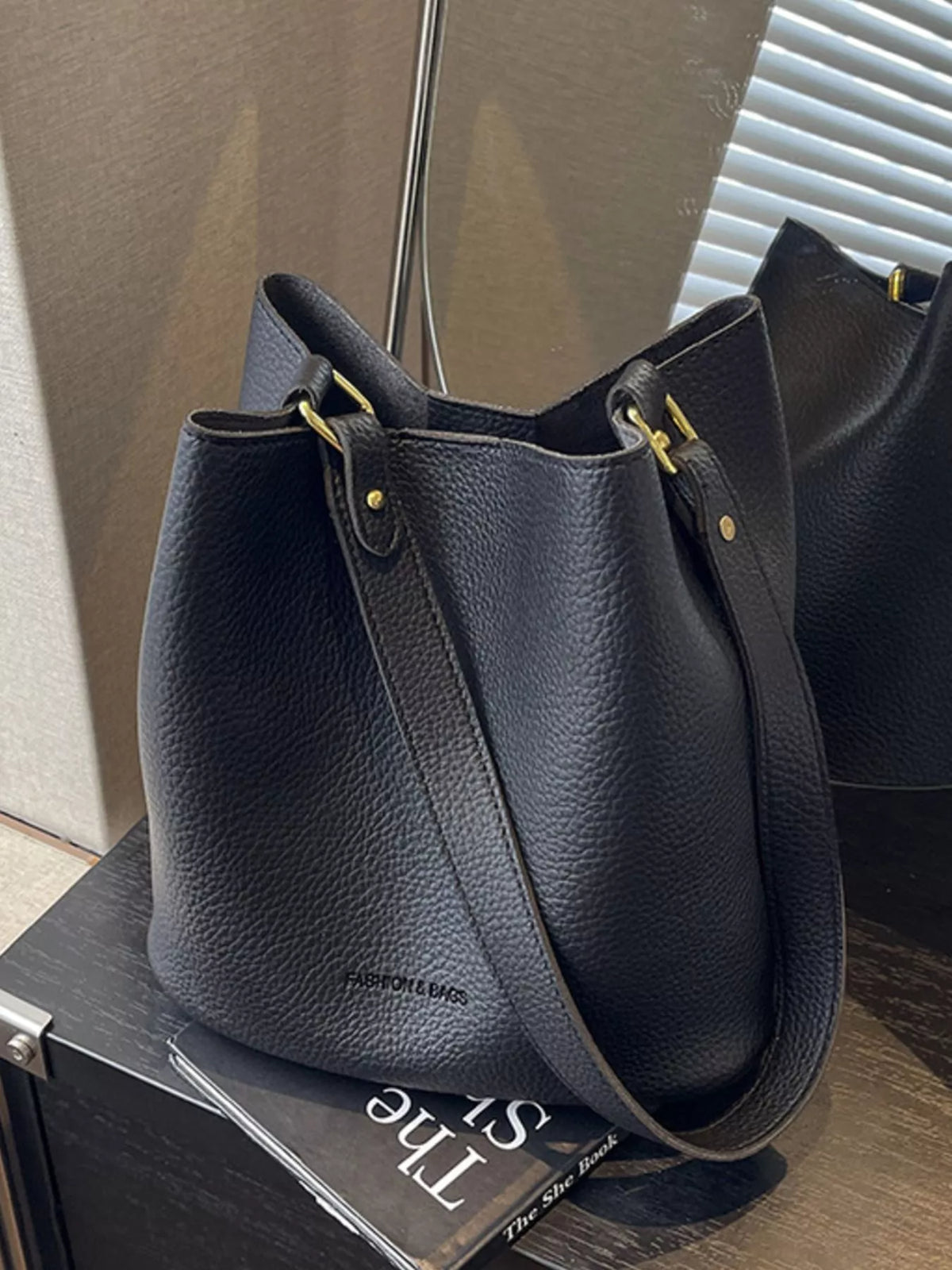 Black pebbled leather tote bag with gold hardware and adjustable strap.