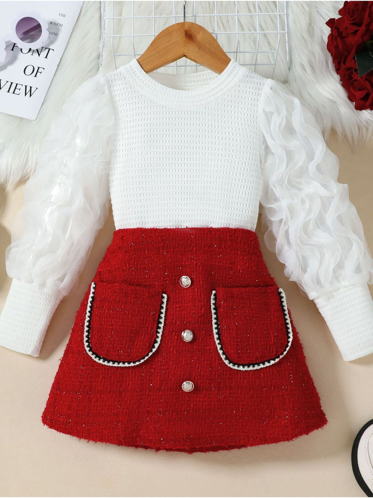 Childrens red tweed skirt with decorative buttons and white textured top with sheer ruffled sleeves.