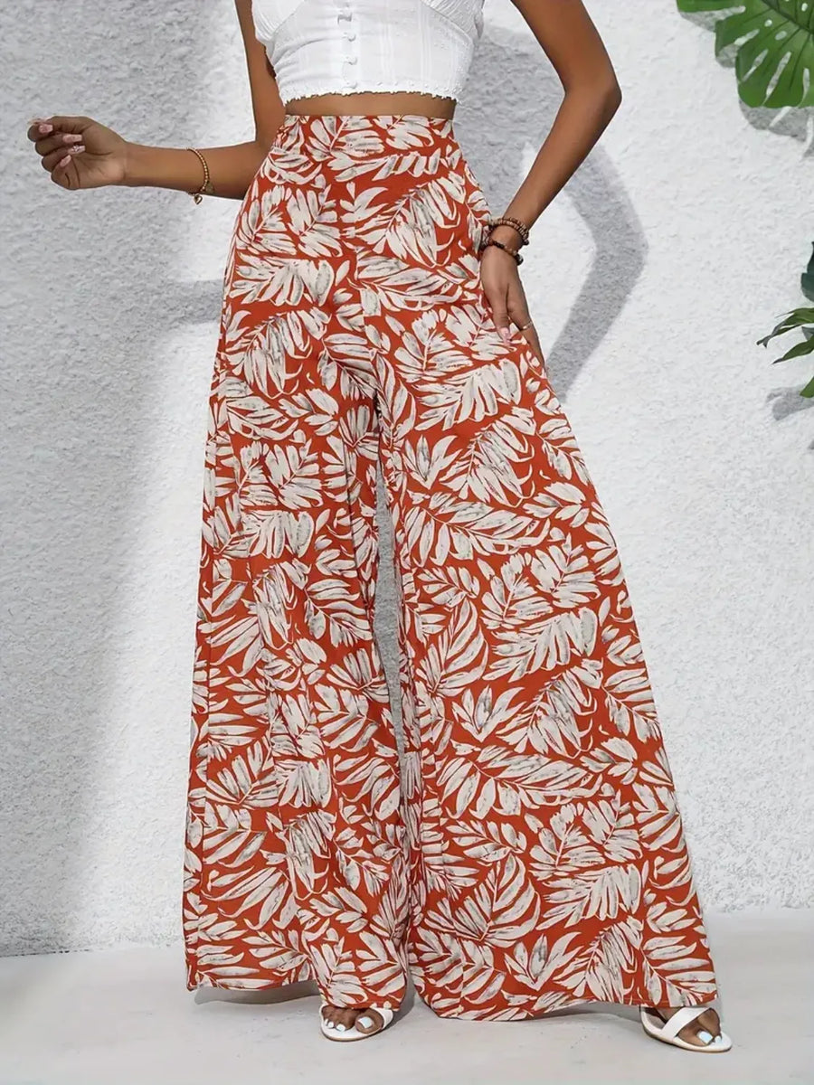 Orange-red palazzo trousers with a white tropical leaf print, made of 100% polyester.