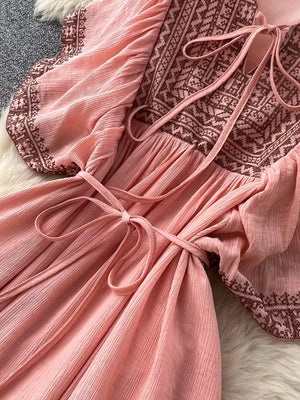 Pink V-neck maxi dress with embroidered yoke and sleeves, tie waist, and textured fabric.