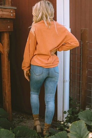 Caramel corduroy sweatshirt with a jack-o'-lantern graphic, styled with denim jeans.