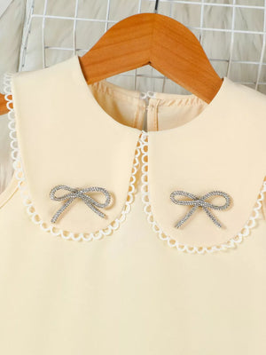 Toddler apricot dress with Peter Pan collar, lace trim, and two jeweled bows.