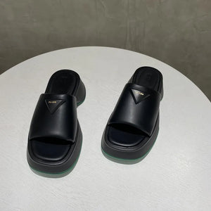 Black geometric platform slides with triangular branding detail and green sole accent.