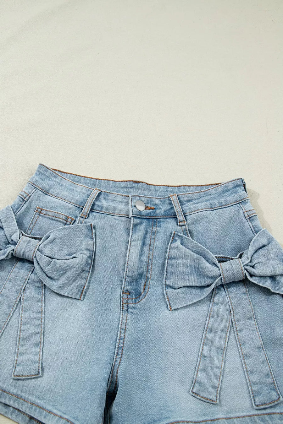 Light wash denim shorts with bow embellishments and button fly.