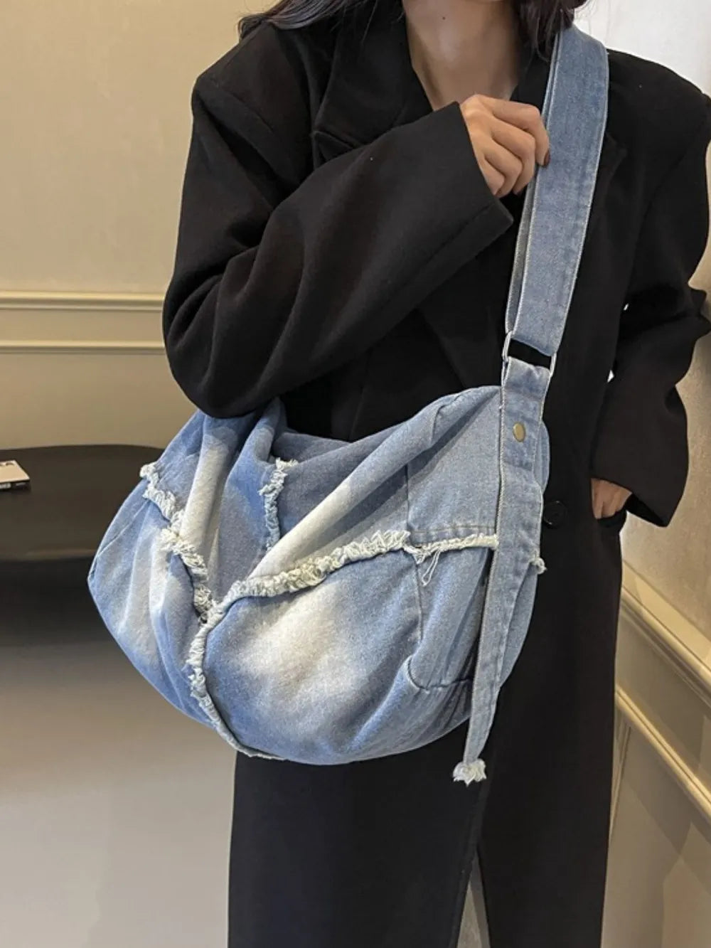 Light wash denim slouch crossbody bag with frayed edges and adjustable strap.