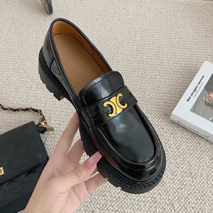 Black patent leather loafers with chunky sole and gold buckle detail.