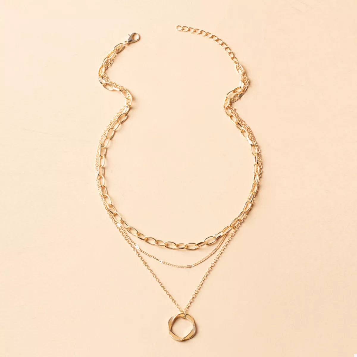 Gold layered necklace with three delicate chains and a geometric pendant.