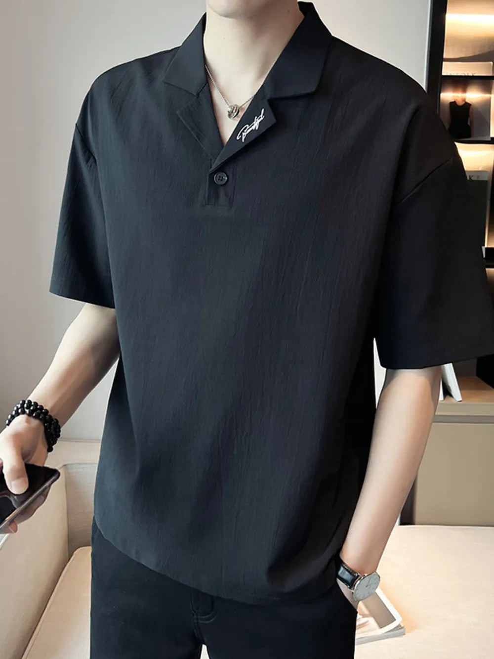 Black cotton polo shirt with button-down collar and embroidered detail.