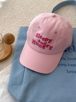 Blush pink baseball cap with "Sleepy And Hungry" embroidered text