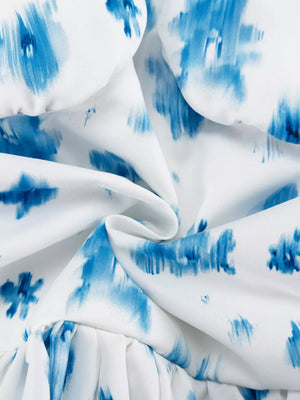 White dress with blue abstract floral print and ruffled hem.