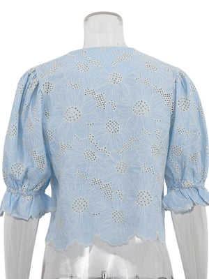 Blue eyelet crop top with white floral embroidery, puff sleeves, and ruffled cuffs.