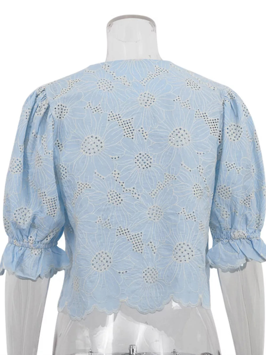Blue eyelet crop top with white floral embroidery, puff sleeves, and ruffled cuffs.