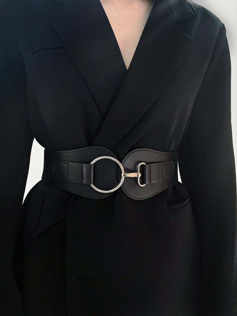 Black cincher belt with a silver ring and buckle closure, styled over a black jacket.