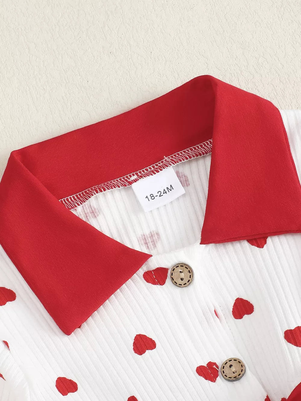 Baby dress with red hearts pattern, white ribbed cotton, red collar, and wooden buttons.