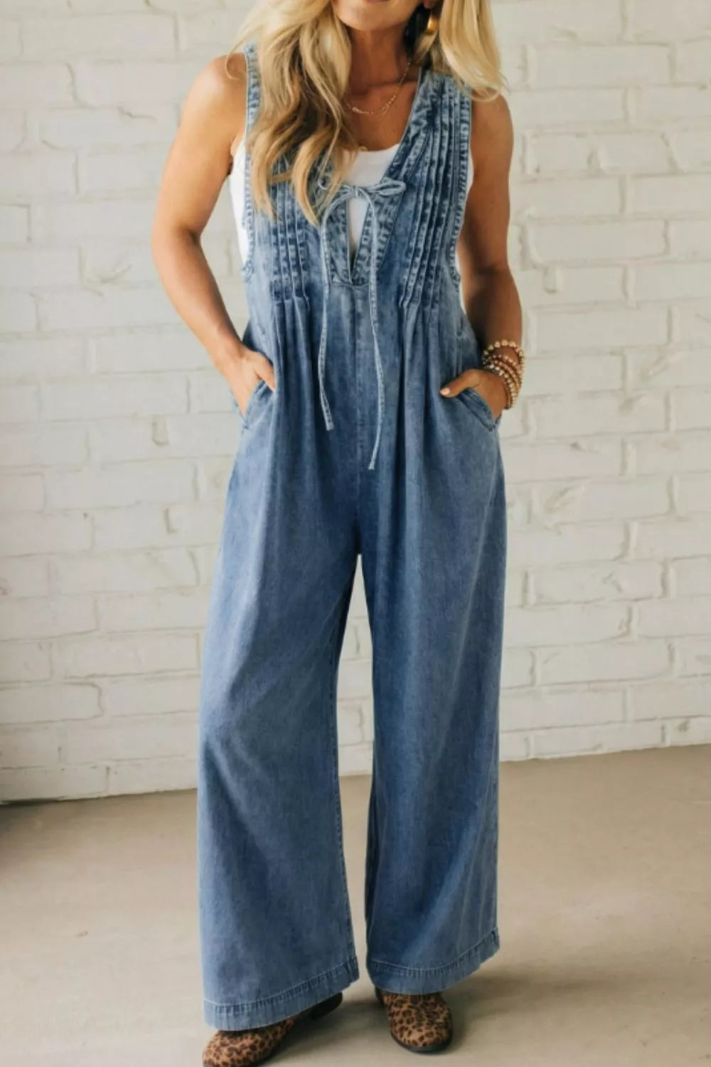 Denim jumpsuit with V-neck, tie detail, pintuck bodice, wide leg, and pockets.