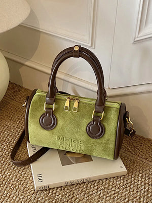 Green barrel crossbody bag with brown trim and handles, gold zippers, and embossed text.