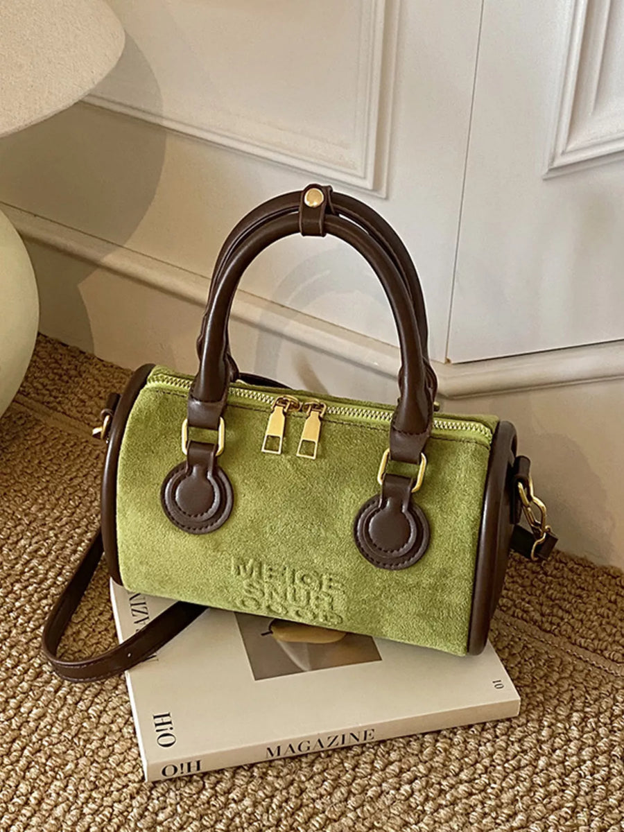 Green barrel crossbody bag with brown trim and handles, gold zippers, and embossed text.