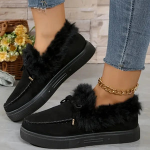 Black suede loafers with shearling trim and decorative tie detail.