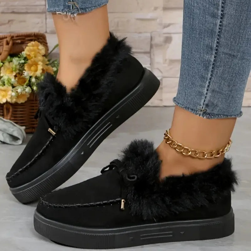 Black suede loafers with shearling trim and decorative tie detail.