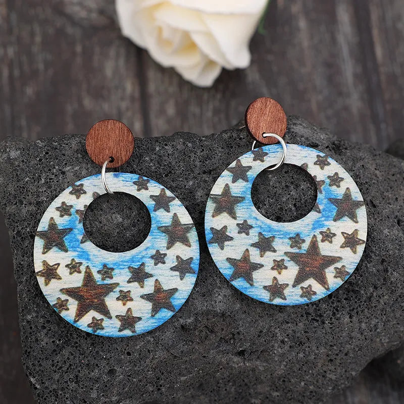 Multicolor celestial starburst wood hoop earrings with brown star pattern on blue sky background.