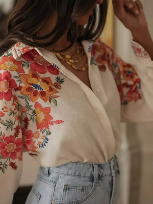White linen shirt with vibrant floral embroidery on collar, shoulders, and sleeves.