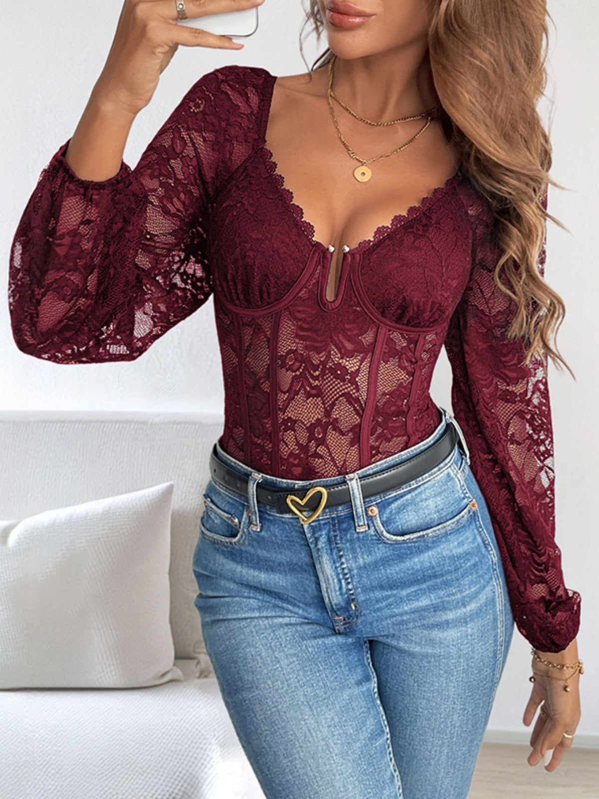 Burgundy lace bodysuit with long balloon sleeves, sweetheart neckline, and corset detail, styled with jeans.