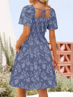 Dusty blue smocked mini dress with tiered floral skirt and tie-back square neck.