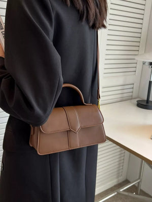 Chic small top handle bag in brown with a flap closure and top handle, styled as a shoulder bag.