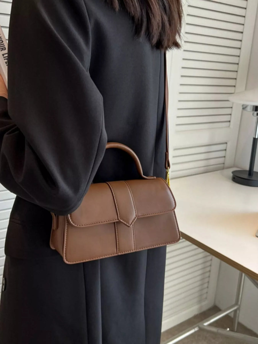 Chic small top handle bag in brown with a flap closure and top handle, styled as a shoulder bag.