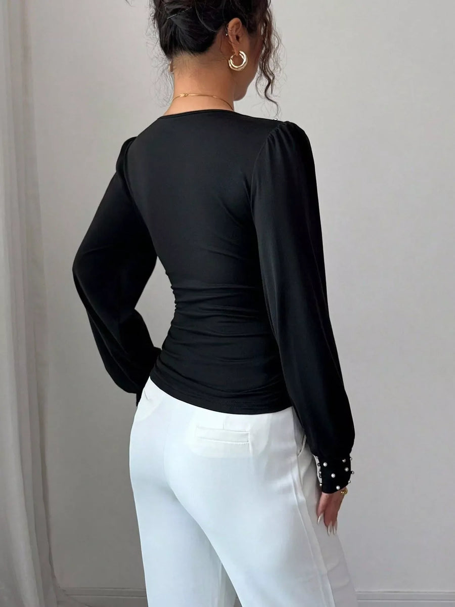 Black ruched V-neck blouse with pearl embellished cuffs and puff sleeves.