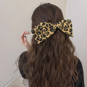 Leopard print oversized hair bow with fabric texture, worn in long wavy brown hair.