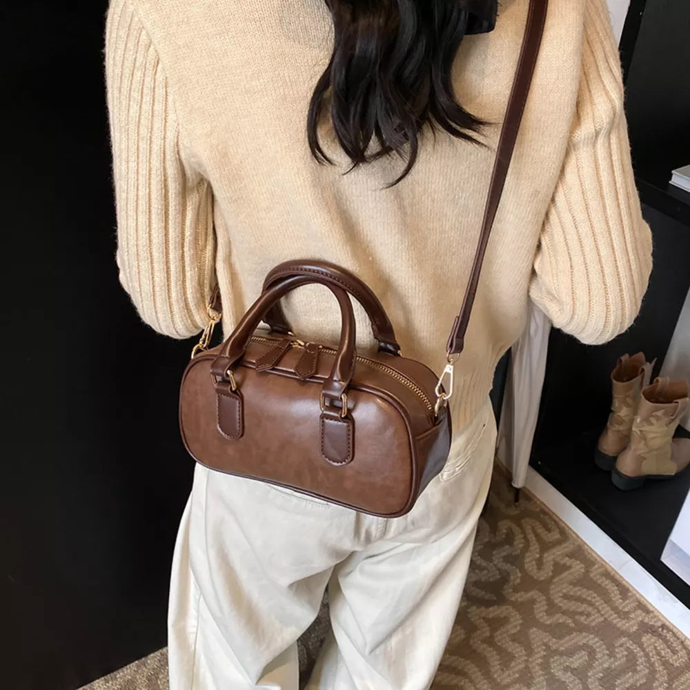 Chic mini barrel crossbody bag in brown faux leather with top handles and adjustable strap.