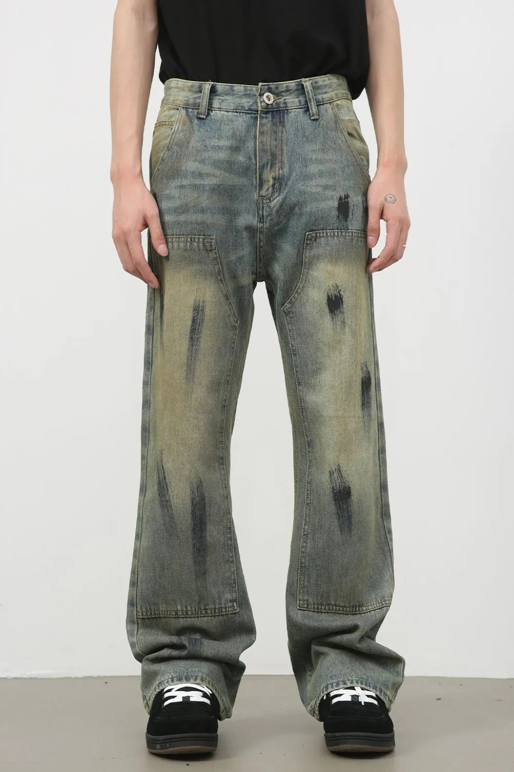 Distressed carpenter jeans in medium wash denim with black paint-like splatters and a relaxed fit.
