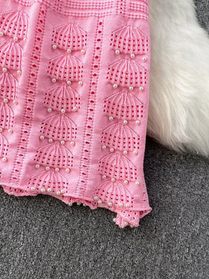 Pink knit midi dress with pearl embellishments and cutout details.