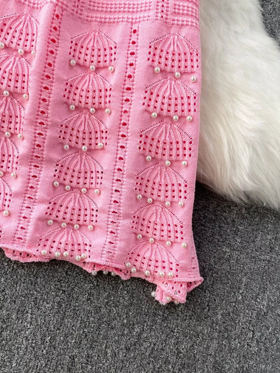 Pink knit midi dress with pearl embellishments and cutout details.