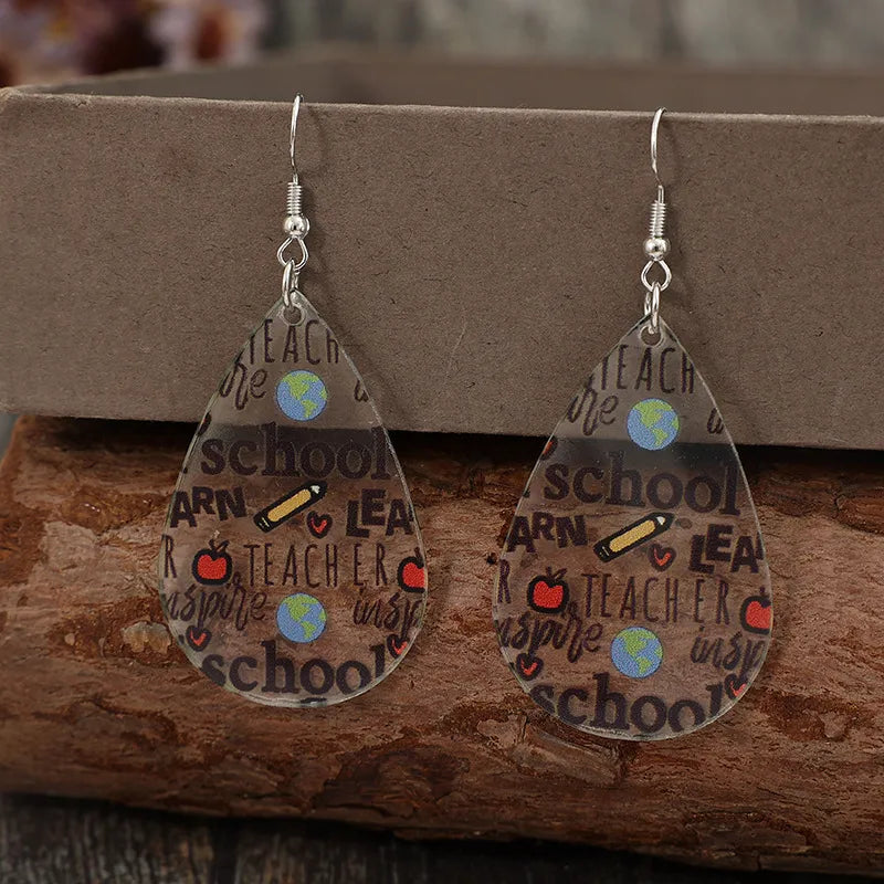Schoolhouse graphic teardrop earrings in transparent acrylic with teacher-themed print.