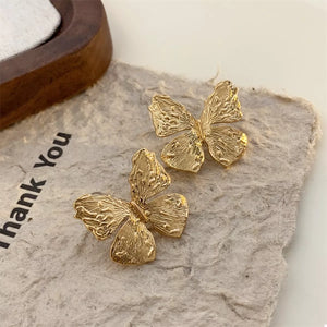 Textured gold-plated butterfly stud earrings with intricate detailing.