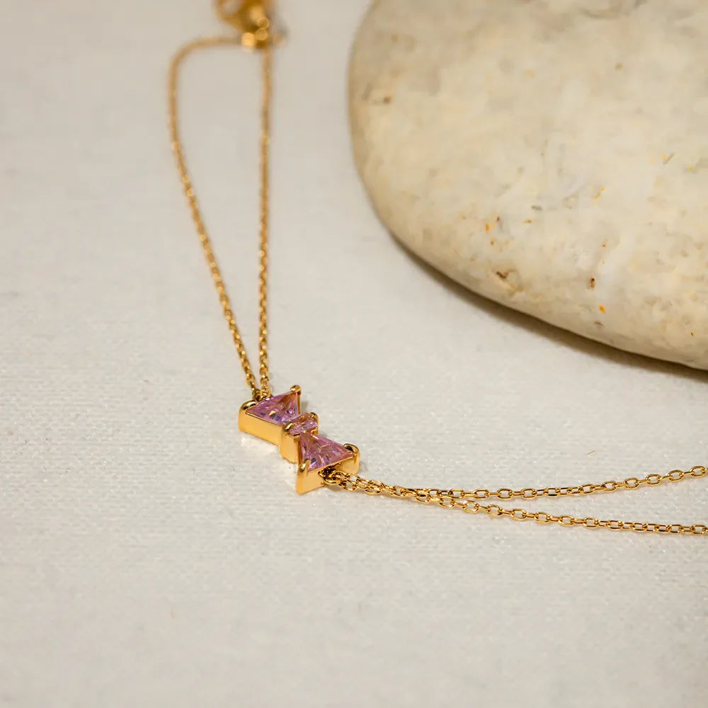 Gold chain bracelet with two pink gemstone bow charms.