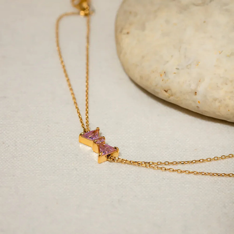 Gold chain bracelet with two pink gemstone bow charms.