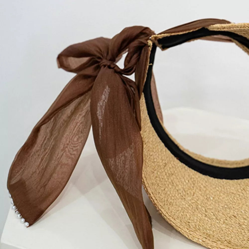 Straw visor hat with coffee ribbon tie and beaded detail.