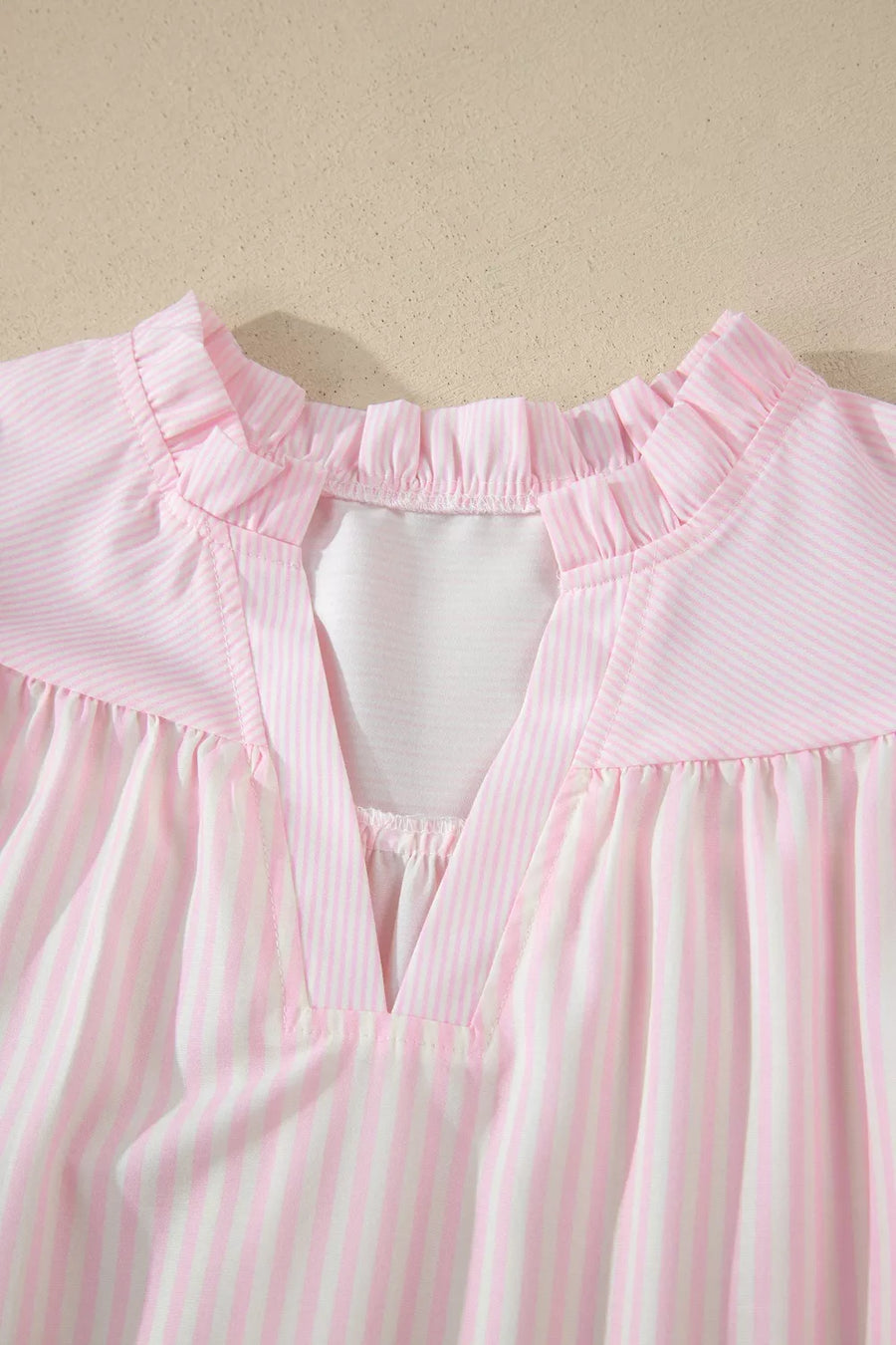 Pink and white striped polyester blouse with ruffled neckline and V-neck detail.
