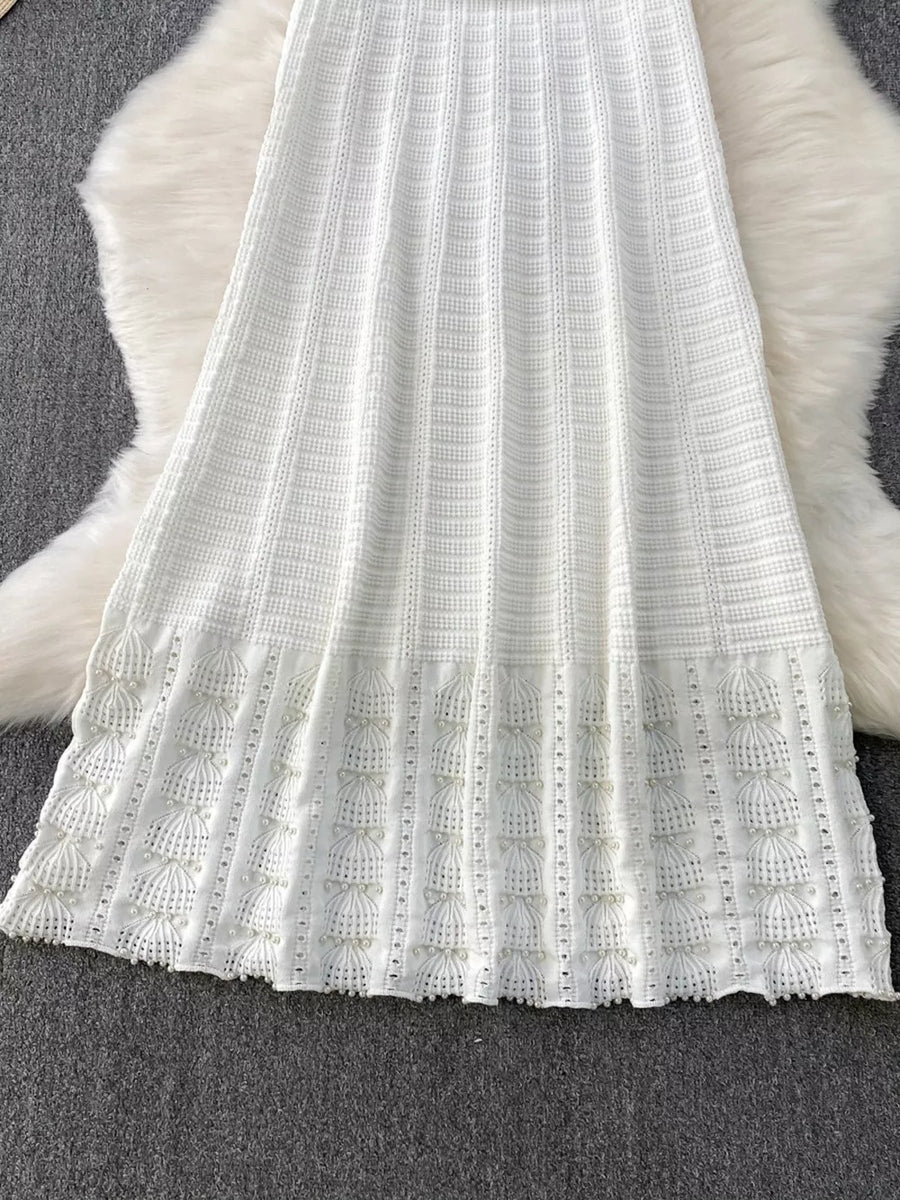 White knit midi dress with textured pattern and pearl-embellished cutout hem detail.