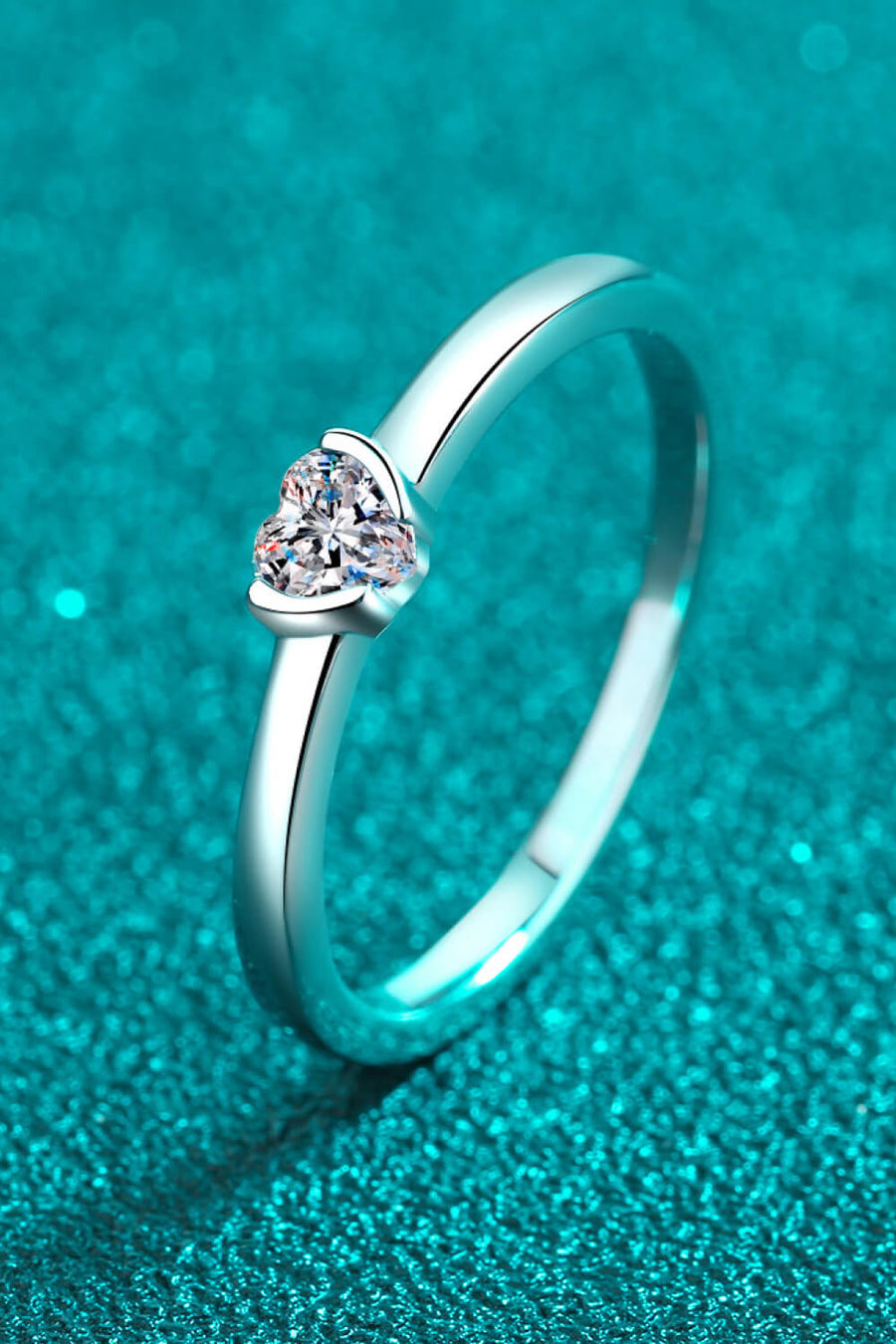 Silver ring with a heart-cut solitaire diamond on a textured teal background.