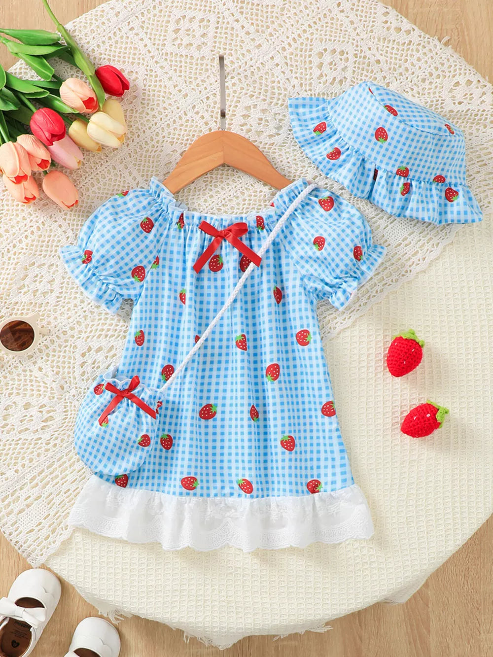 Baby dress set with blue gingham and strawberries, puff sleeves, red bow, and lace trim.