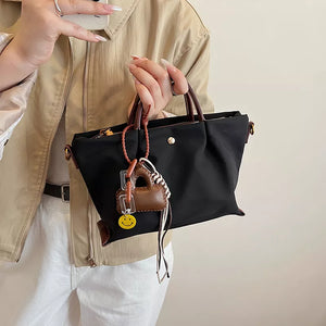 Compact black nylon handbag with brown leather accents and playful charms.