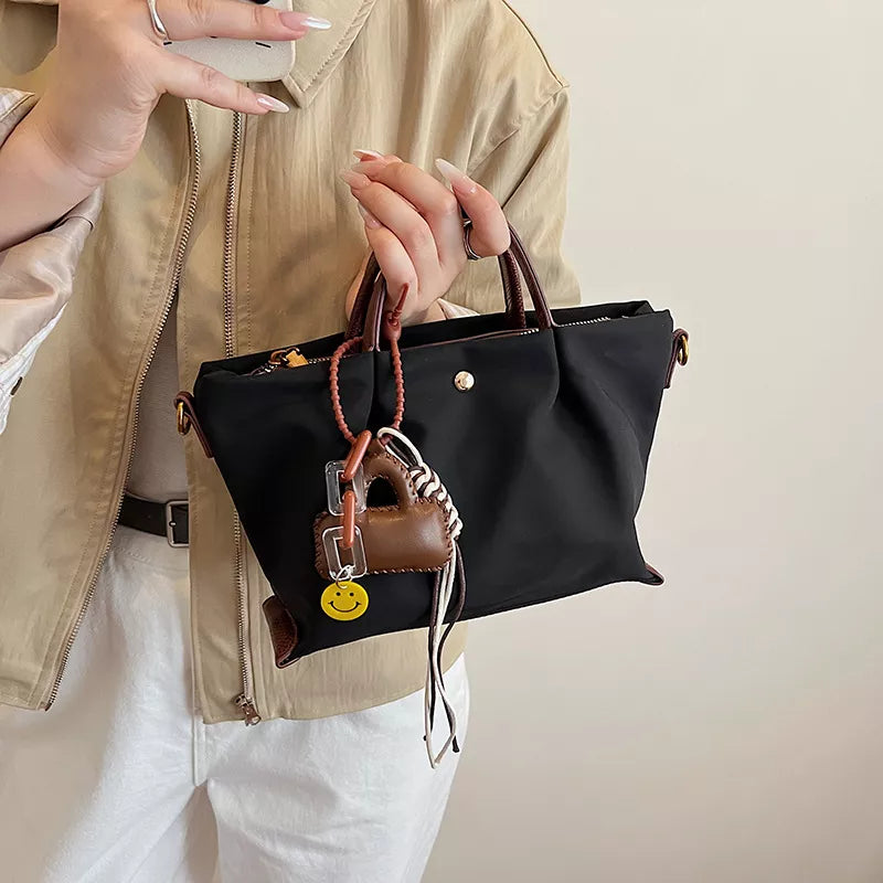 Compact black nylon handbag with brown leather accents and playful charms.
