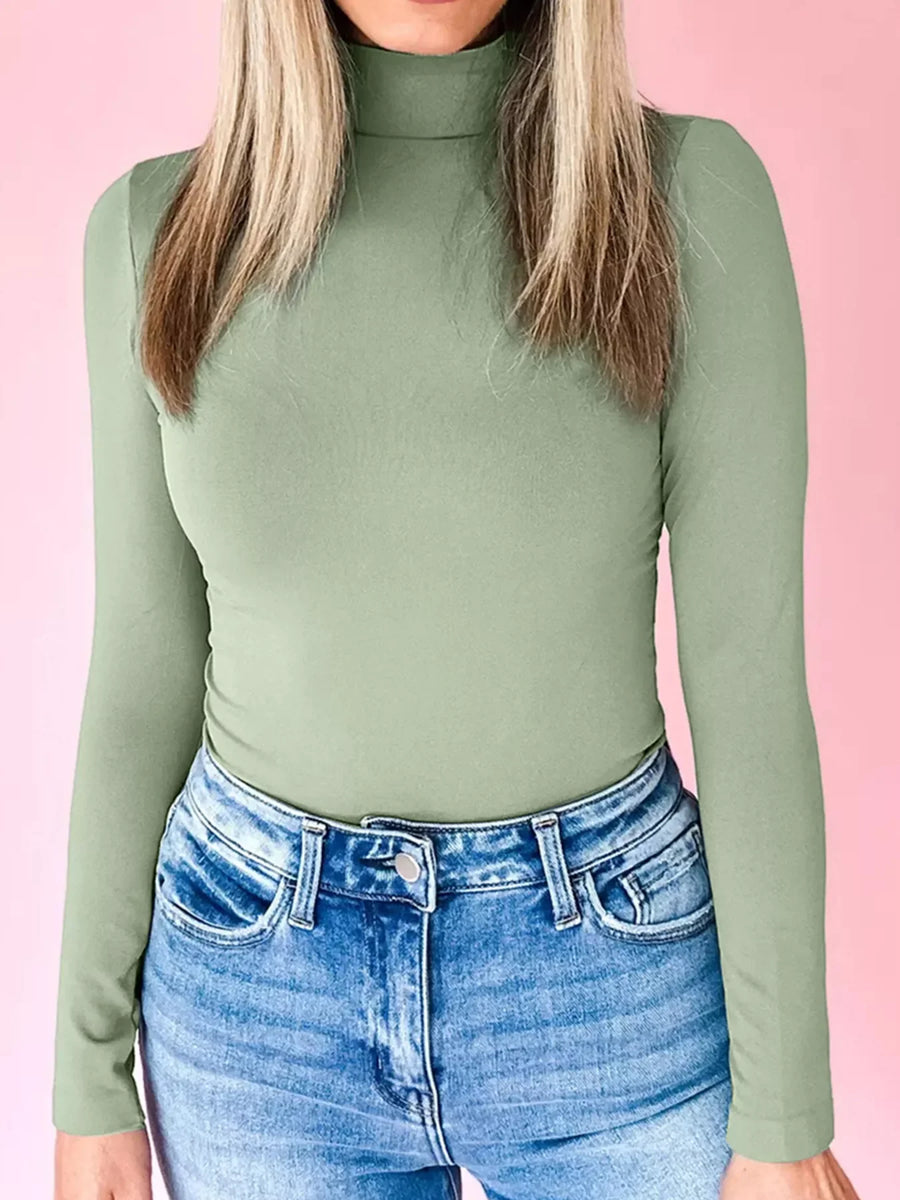 Stretchy long-sleeve turtleneck tunic in sage green, styled with blue jeans.